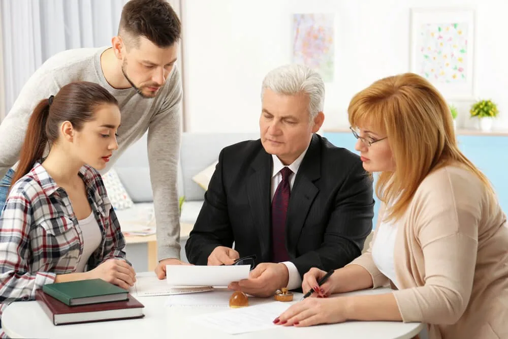 An adviser in a suit going through paperwork at a table with a family.